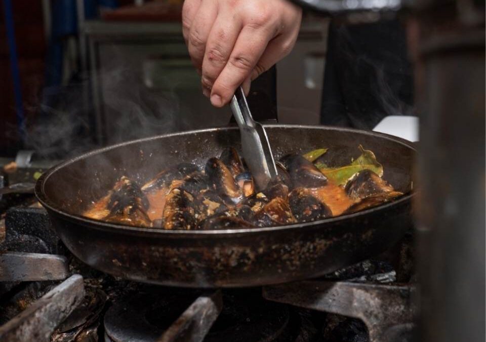 Cocinero preparando un plato sobre el fuego en la cocina del Restaurante El Pote, mostrando sus especialidades tradicionales